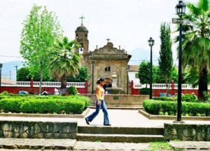 A young girl dashes across the plaza of Cuanajo. In the background, the parish church overlooks a fountain.