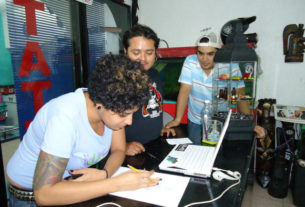 A graduate in Fine ARts, Angy works on a drawing at her tattoo parlor in Oaxaca, Mexico. Her partners look on. © Alvin Starkman, 2011